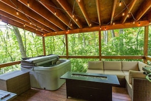 Covered porch off kitchen and living room with hot tub, outdoor seating, firetable, and propane grill