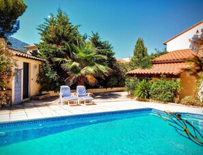 Looking across the pool with poolhouse on left, & shower. 2 sunloungers. Canopy