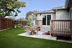 Back yard with patio furniture, cafe lighting, and artificial turf.