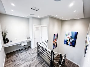 Work or relax in this bright, serene space featuring a dedicated office nook with a sleek desk and comfortable chair, complemented by vibrant modern artwork and plenty of natural light, making it the perfect spot for productivity or inspiration