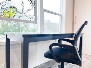Find inspiration in this bright and peaceful workspace, featuring a modern desk and ergonomic chair, with natural light streaming through the window and a beautiful stained-glass design to add a touch of creativity