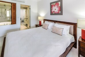 The primary bedroom offers a king-sized bed and connects to an open-air ensuite with a glass shower and jetted spa bath.
