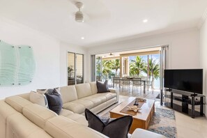 A spacious living area highlights an oversized L-shaped couch where you can watch TV or open the wall-to-wall bi-fold doors and step outside to the private balcony.