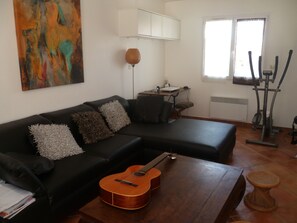 salle à manger avec télé, guitare, coin bureau et vélo elliptique