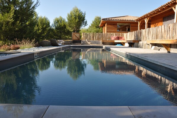 Vue depuis la piscine, maisonnette au fond et maison principale à droite.