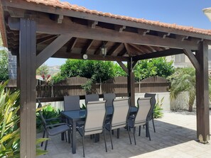 Outdoor dining table with seating for 8, covered by a large gazebo.