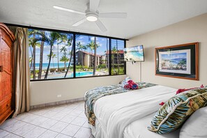Experience breathtaking ocean and resort pool views from this stylish bedroom, offering a cozy atmosphere and a TV for entertainment.