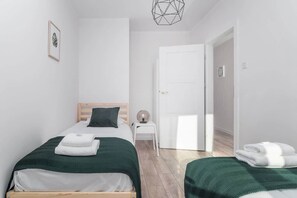 Bedroom with two single wooden beds with white linen and green bedspread.