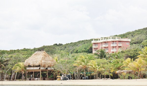 View of beach and palapa with condo resort in background.