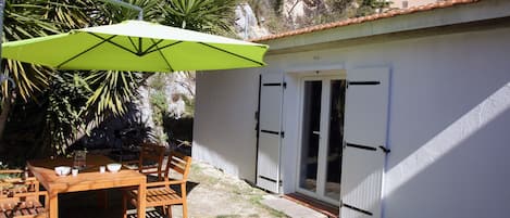 Entrée du cabanon avec la table, les chaises, le parasol et le barbecue.