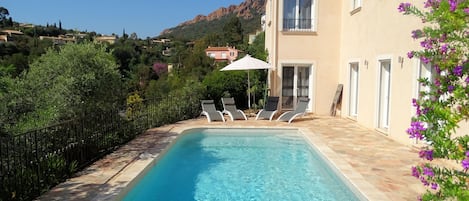 Grande piscine ensoleillée avec bains de soleil, parasol et coin détente