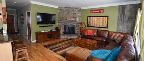 living room has a large wraparound couch and a 65 inch 4K TV and gas fireplace.
