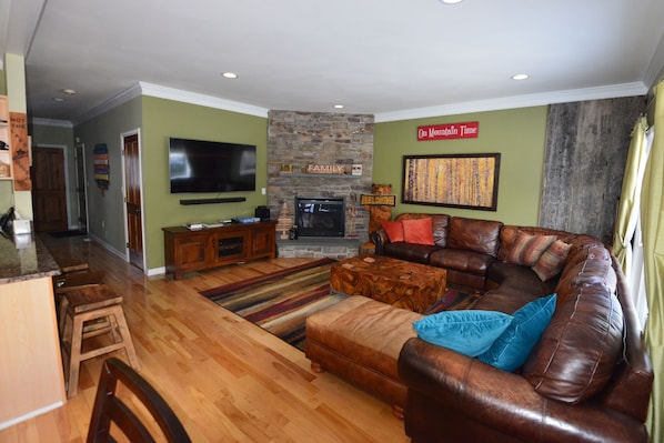  living room has a large wraparound couch and a 65 inch 4K TV and gas fireplace.