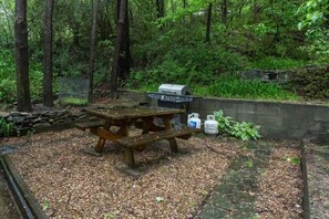 On the stone patio is a picnic table and gas grill
