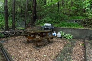 On the stone patio is a picnic table and gas grill