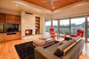 Cosy up in the spacious living room, featuring a striking stone fireplace, plush seating, and floor-to-ceiling windows that frame breathtaking valley views.