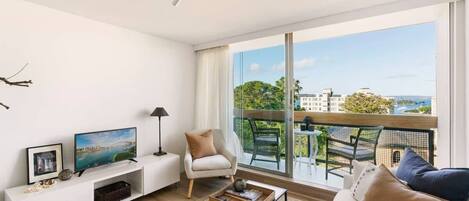 Our lovely, comfy living space with balcony + view of our charming neighborhood and the ocean!