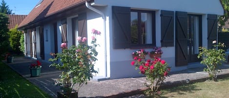 Front of house with south-facing patio and small grass lawn to  hedge