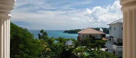 A picturesque balcony retreat offering serene sea views, accented by ornate pillars and a tapestry of tropical flora