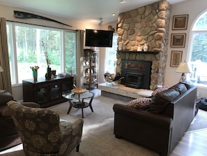 Main living room with wood fireplace, surrounded by windows to enjoy the beauty