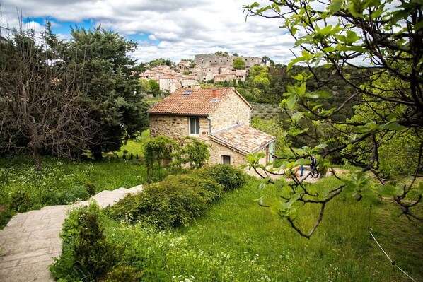 Vue de la maison depuis le chemin pavé, le château et la plaine en fond.