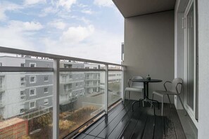 A small balcony with glass railings and a view of nearby buildings, providing a cozy outdoor space for relaxation.