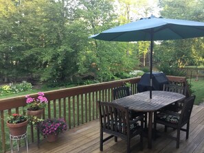 Deck with grill looks out onto lawn and small wooded area