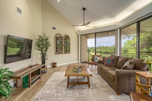Relax in a spacious living room with floor-to-ceiling windows, offering a serene view of the balcony and tropical greenery. Perfect for unwinding after a day in Lahaina.