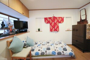 Single futon bed with TV, books and decorative red kimono on wall