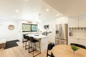 modern kitchen features white shaker cabinets, quartz countertops, stainless steel appliances, and a spacious island with seating.