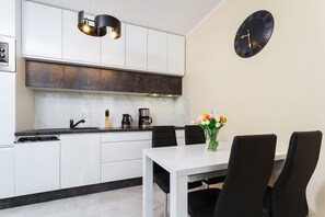 A small dining area with a table and chairs, alongside a minimalist kitchen with modern black and white decor.