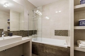 A modern bathroom with a bath with glass panel, and light-colored tiles.