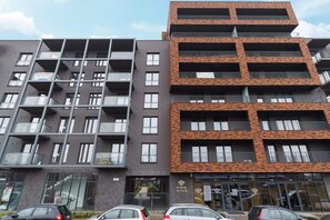 An exterior view of a modern apartment building with a red brick and black facade, featuring balconies.