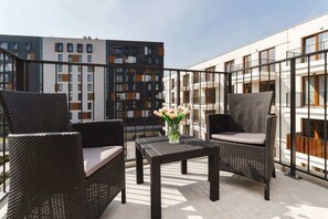 A modern outdoor balcony with a black dining set, including chairs and a table, offering a relaxing space with a view of a contemporary residential building.