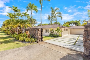 Welcoming home entrance with tropical landscaping and a spacious driveway.