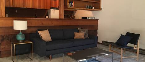 The living room with new sofa, leather chair, and tables. Galley kitchen beyond.