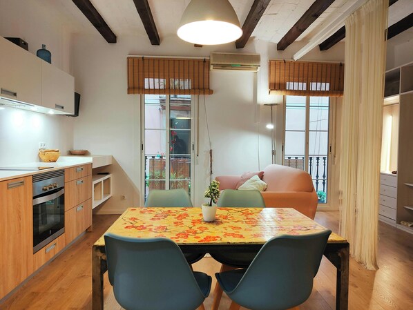 The dining area features a wooden table surrounded by four chairs.  A glimpse of the modern kitchen can be seen in the background, with its wooden cabinets and sleek appliances.