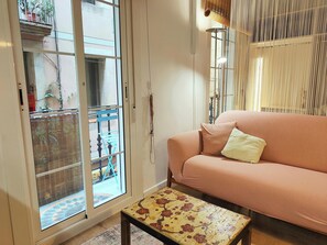 Natural light streams into this trendy Barcelona loft, illuminating a stylish living space designed for relaxation and urban exploration. The blend of modern furnishings and glimpses of traditional Spanish architecture through the balcony door creates a u
