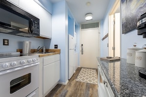 Observing from within the unit's hallway reveals a compact kitchen equipped with a microwave, refrigerator, and a convenient washer & dryer setup.