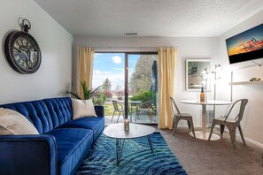 A versatile full futon sofa bed paired with a dining table for two, accompanied by a smart TV, and granting access to a charming balcony.