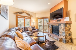 Living area with mounted flat screen TV, gas fireplace, ample seating and balcony access.