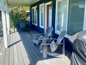 Large covered deck with dining table, propane barbecue and Adirondack chairs.