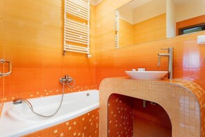 A bathroom designed with orange tiles, a bathtub, and modern fixtures, adding warmth to the space.