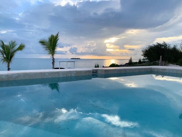 Coral Point's ocean view pool with ocean and sunset views. Dock is visible beyond it.