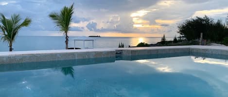 Coral Point's oceanview pool with ocean and sunset views.  Boat dock is visible beyond it.