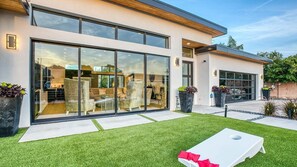 Modern single-story home with sliding glass doors, turf, and twilight glow.