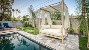 Serene backyard with canopied daybed, pool, lounge chairs, and greenery.
