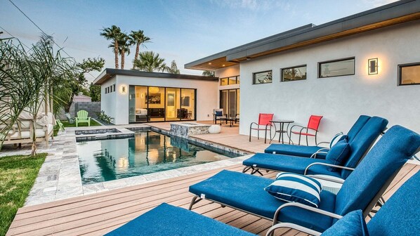 Modern backyard with pool, lounge chairs, fire pit, and lush landscaping.
