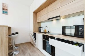A sleek, modern kitchen with wood accents and white cabinetry. It’s small but functional, with essential appliances.