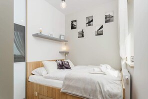 Compact bedroom with a simple bed, bedside lamp, and wall decor. The space feels warm and inviting with neutral tones.